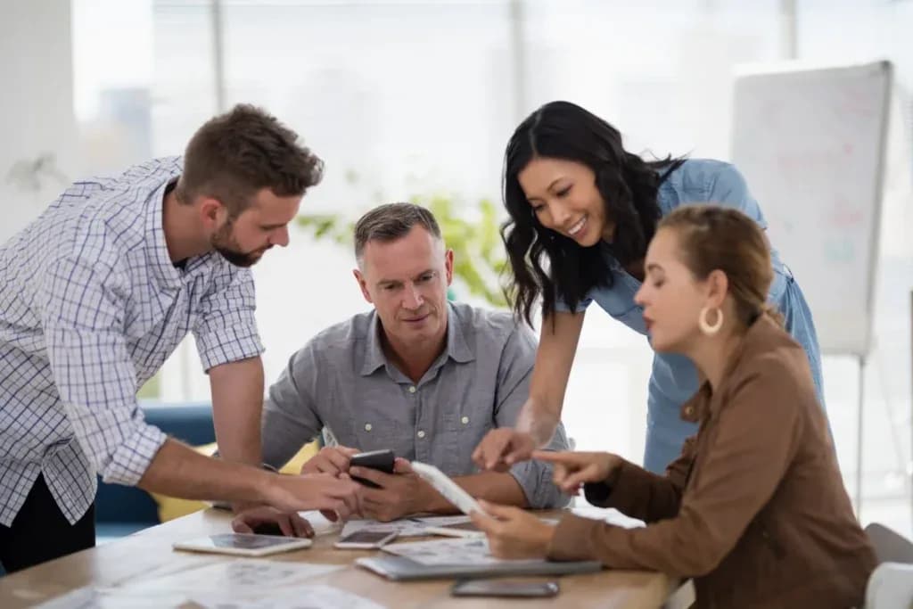 Four colleagues around a desk reviewing printed charts together
